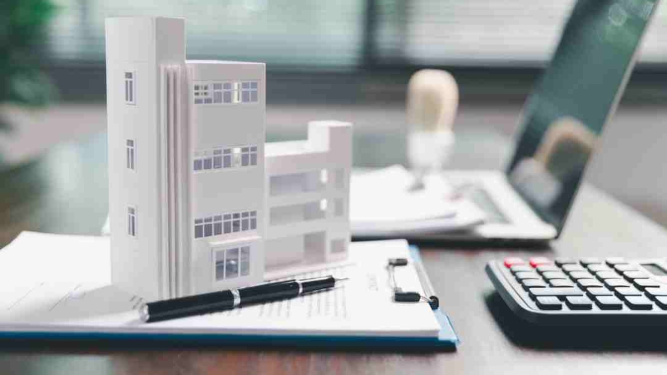 Model of an apartment building on a contract, with a calculator and laptop.