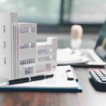 Model of an apartment building on a contract, with a calculator and laptop.